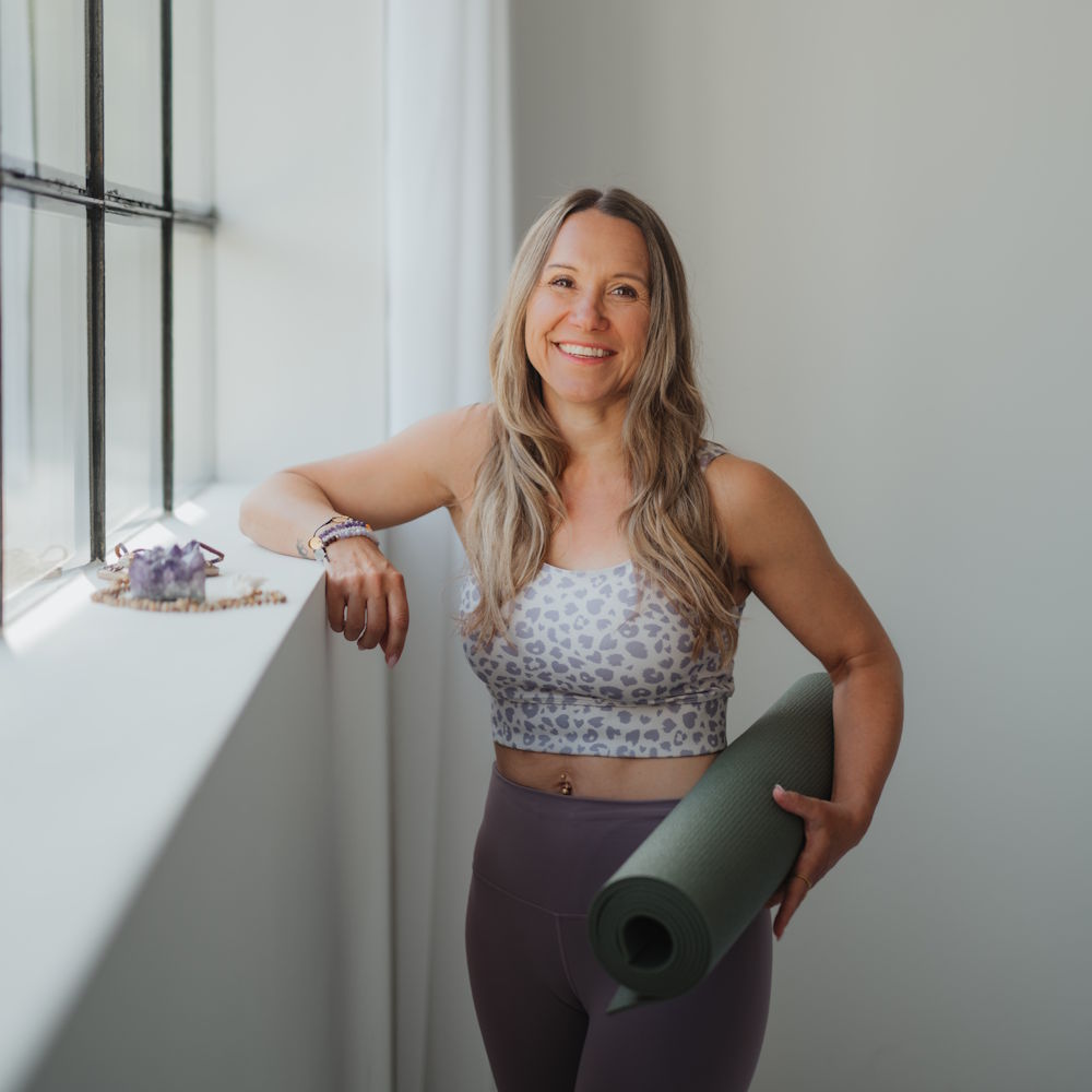 Yoga-Trainerin mit Yogamatte am Fenster im hellen Kursraum