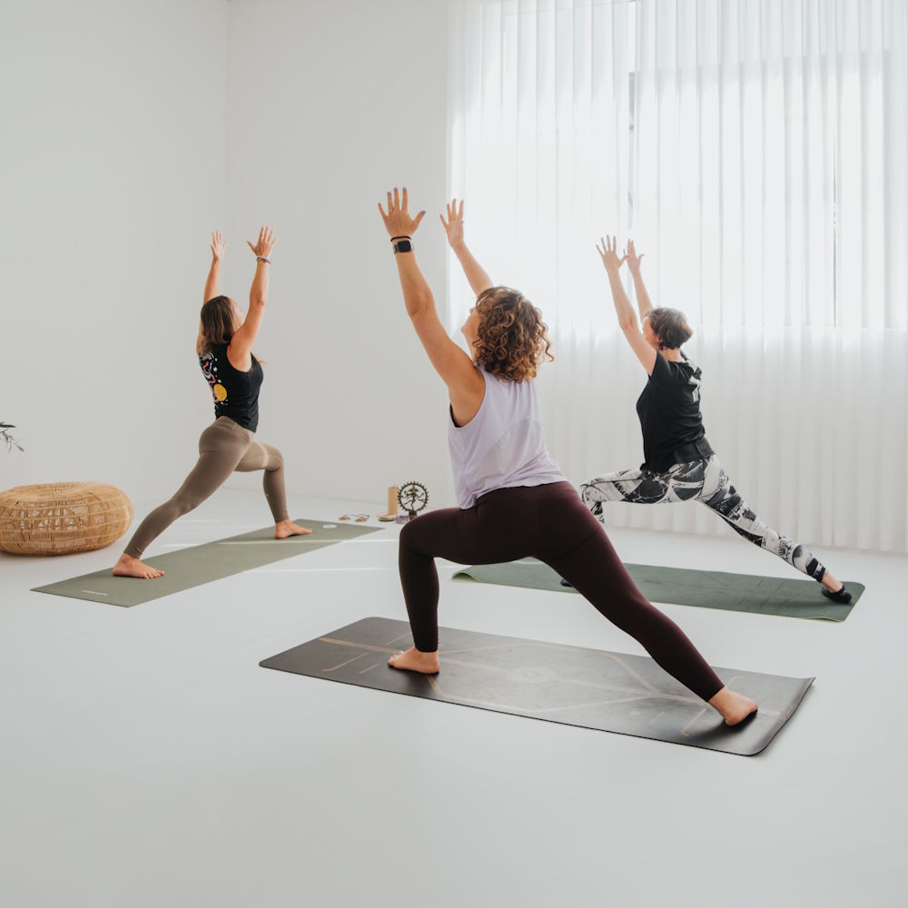 Teilnehmer eines Yogakurses in einer dynamischen Standhaltung auf Yogamatten
